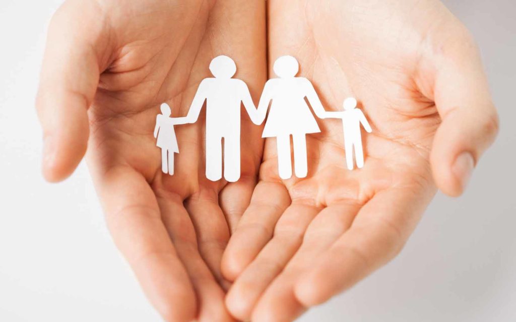 An image of Caucasian hands holding paper silhouettes of a man, women and two children