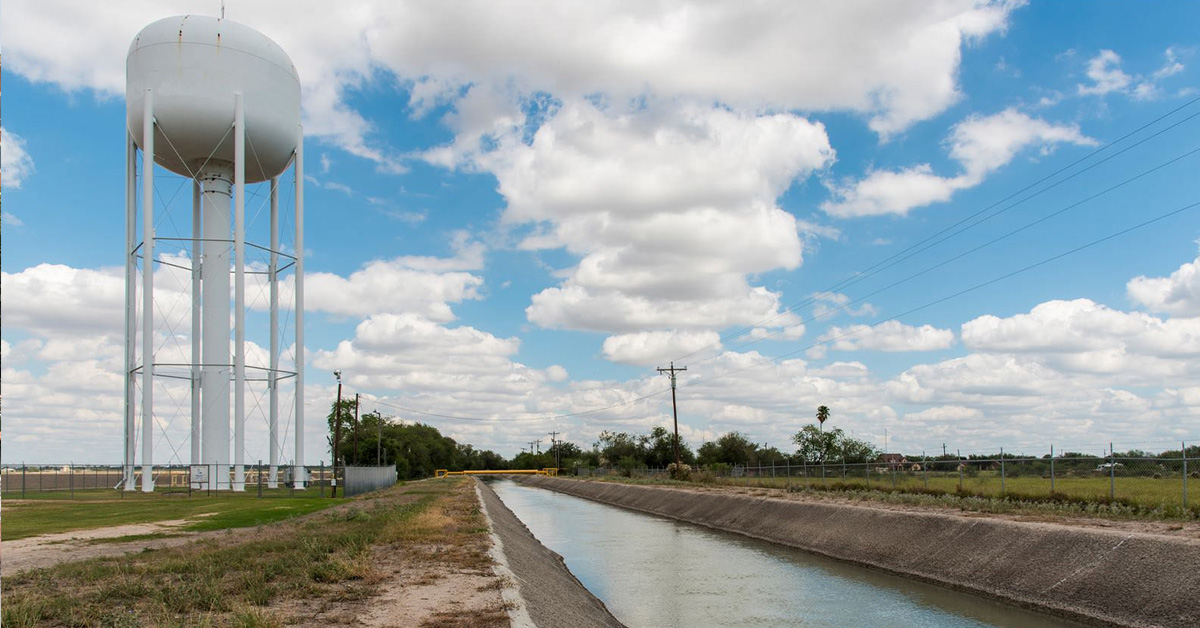 White water tower sight in a field with a reservoir to the right and clouds overhead
