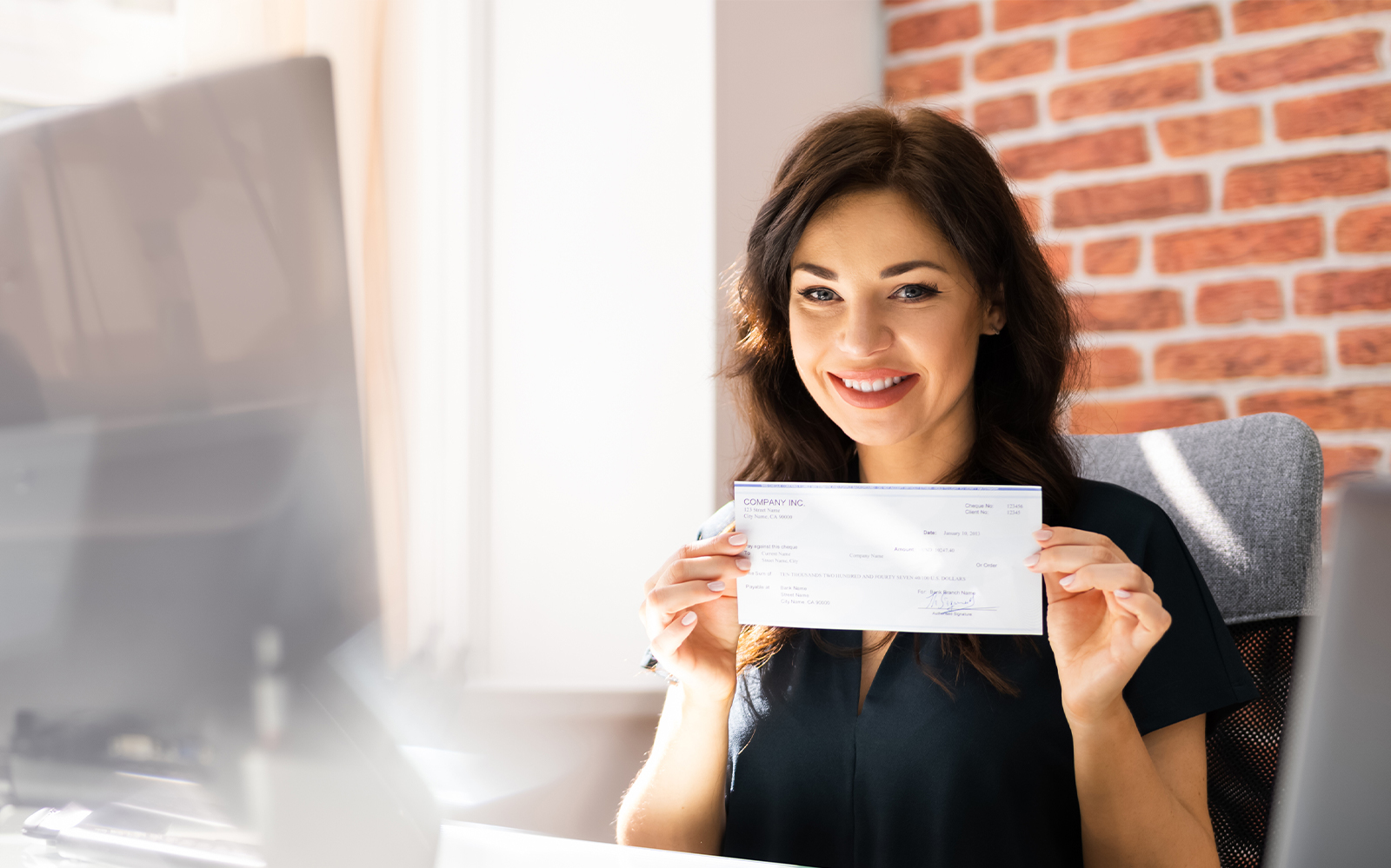 woman sitting at desk holding a check