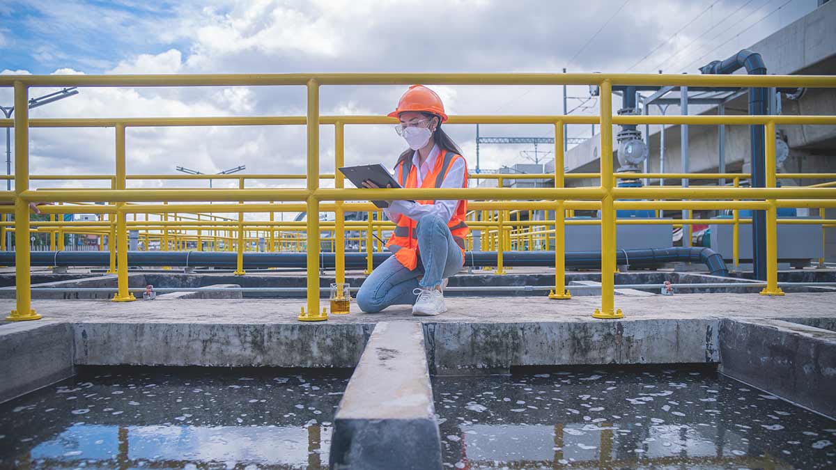 Worker taking water from the wastewater treatment pond to check the quality of the water
