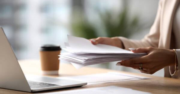 stack of paperwork on a desk with laptop