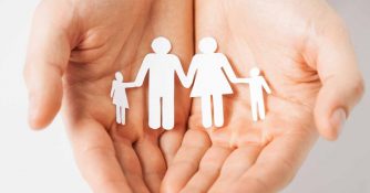 An image of Caucasian hands holding paper silhouettes of a man, women and two children